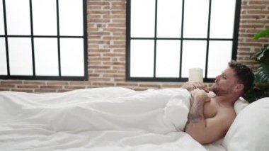 Young caucasian man waking up stretching arms at bedroom