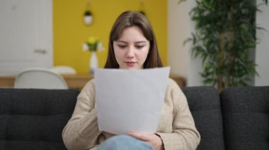 Evinde sürpriz ifadesiyle doküman okuyan genç sarışın kadın.