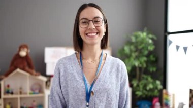 Young beautiful hispanic woman teacher smiling confident standing with arms crossed gesture at kindergarten