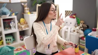 Young beautiful hispanic woman preschool teacher asking for silence at kindergarten