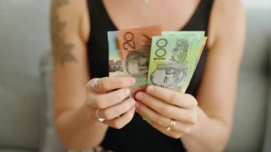 Avustralya doları sayan genç bir kadın evde banknot sayıyor.