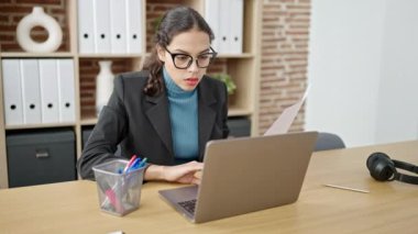 Young beautiful hispanic woman business worker using laptop reading document at office