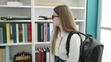 Üniversite sınıfında akıllı telefon kullanarak kitap arayan genç sarışın kız öğrenci.