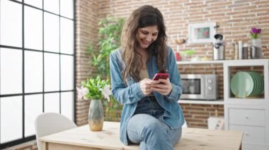 Genç, güzel, İspanyol bir kadın yemek masasında akıllı telefon kullanıyor.