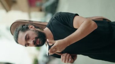 Young hispanic man musician talking on smartphone holding guitar case at street
