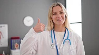 Genç sarışın kadın doktor klinikte başparmağını kaldırıyor.