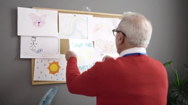 Senior Trabajando Como Profesor Colgando Dibujar Tablero Corcho Jardín Infantes — Vídeo de stock