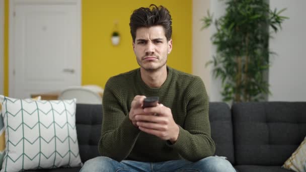 Young Hispanic Man Watching Sitting Sofa Boring Expression Home — Wideo stockowe