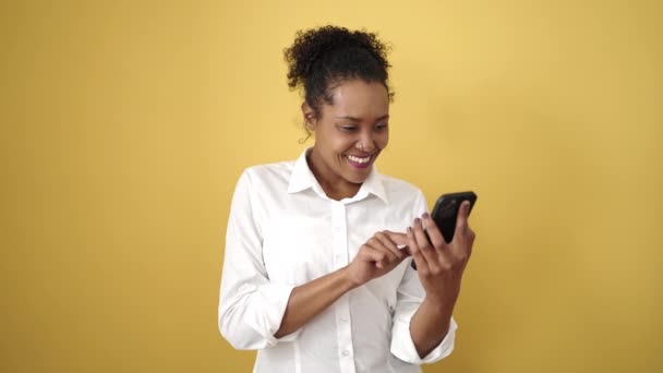 アフリカ系アメリカ人の女性は 孤立した黄色の背景にスマートフォンを使って自信を笑顔 — ストック動画