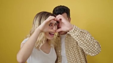 Kadın ve erkek, izole edilmiş sarı arka planda kalp hareketi yapıyor.