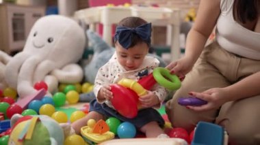 Anaokulunda öğretmenler ve anaokulu öğrencileri masada oyuncaklarla oynuyorlar.