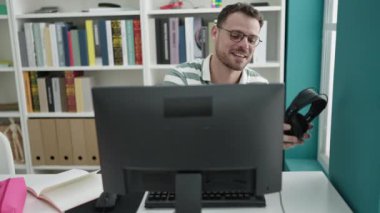Kütüphane üniversitesinde, kulaklık takmış genç bir beyaz adam video görüşmesinde konuşuyor.