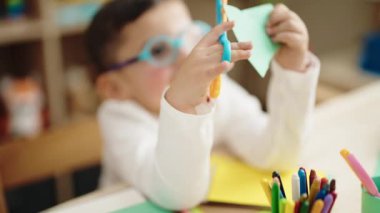 Adorable hispanic boy student smiling confident cutting paper at kindergarten