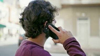 Young hispanic man talking on smartphone with serious expression at street