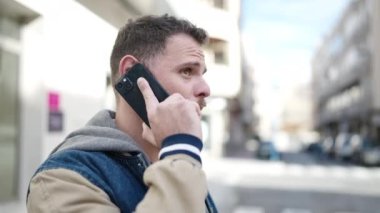 Beyaz bir adam caddede telefonla konuşuyor.