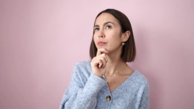 Young beautiful hispanic woman standing with doubt expression over isolated pink background