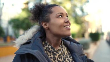 Afro-Amerikalı kadın gülümsüyor, parkın kenarına bakıyor.