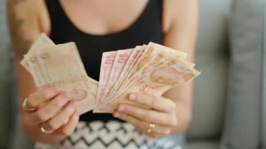 Genç bir kadın evde hindi lira banknotları sayıyor.