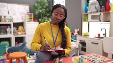 African woman working as teacher writing on clipboard at kindergarten