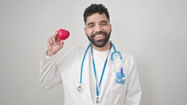 Genç İspanyol doktor gülümsüyor kalbi soyutlanmış beyaz arka planda tutuyor.