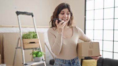 Genç, güzel, İspanyol bir kadın yeni evinde akıllı telefon paketi ile sesli mesaj gönderiyor.