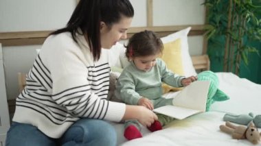 Kadın ve bebek, yatak odasında oturmuş masal kitabı okuyorlar.