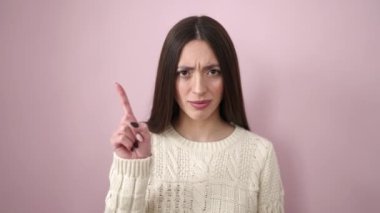Young beautiful hispanic woman standing with relaxed expression doing no gesture with finger over isolated pink background
