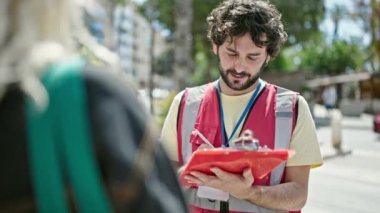 Latin kökenli genç bir adam sokak panosunda anket röportajı yazıyor.