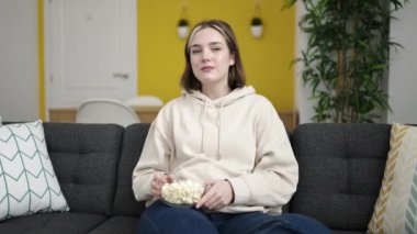 Evdeki kanepede oturup film izleyen genç sarışın kadın.