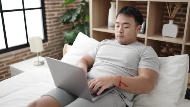 Young Chinese Man Using Laptop Sitting Bed Bedroom — Stock Video