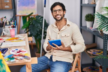 Resim stüdyosunda dokunmatik ped kullanarak gülümseyen genç İspanyol sanatçı.
