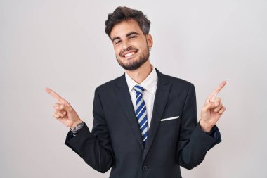 Dövmeli, takım elbiseli ve kravatlı, kendine güvenen, parmakları farklı yönleri gösteren genç İspanyol bir adam. reklam için kopyalama alanı 