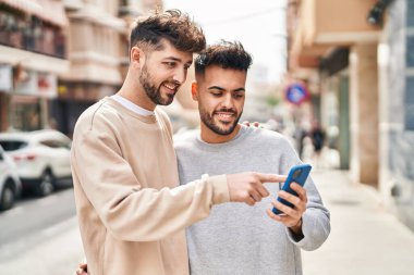 Young couple using smartphone hugging each other at street