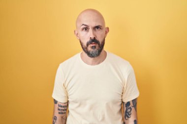 Sarı arka planda dikilen İspanyol dövmeli adam. Uykulu ve yorgun görünüyor. Yorgun ve akşamdan kalma.. 