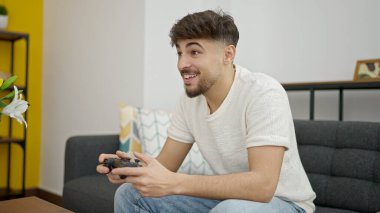 Genç Arap adam video oyunu oynuyor. Evdeki kanepede oturuyor.