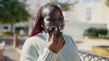 Örgülü saçlı Afrikalı kadın parkta akıllı telefonuyla sesli mesaj gönderiyor.