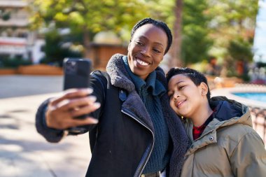 Afro-Amerikan anne ve oğlu gülümsüyor. Parktaki akıllı telefondan özçekim yapıyorlar.