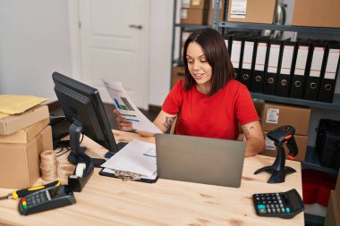 Young beautiful hispanic woman ecommerce business worker using laptop reading document at office