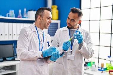 Two men scientists writing on document holding test tube at laboratory