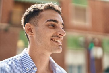 Young hispanic man smiling confident looking to the side at street