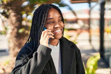 Afro-Amerikalı kadın gülümsüyor. Parktaki akıllı telefondan konuşuyor.