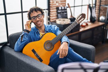 Genç İspanyol müzisyen klasik gitar çalıyor. Müzik stüdyosunda akıllı telefondan konuşuyor.