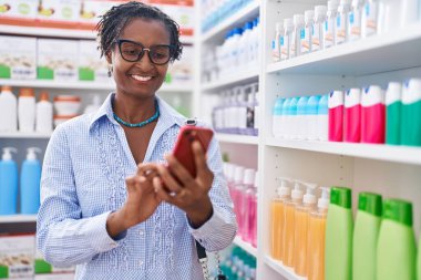 Orta yaşlı Afro-Amerikan kadın müşteri eczanede akıllı telefon kullanarak gülümsüyor.