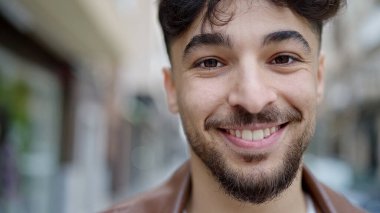 Genç Arap adam sokakta kendine güvenerek gülümsüyor.
