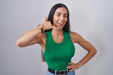 Young woman standing over isolated background smiling doing phone gesture with hand and fingers like talking on the telephone. communicating concepts. 