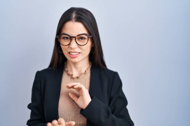 Young brunette woman standing over blue background disgusted expression, displeased and fearful doing disgust face because aversion reaction. with hands raised 