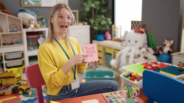 Young blonde woman preschool teacher teaching vocabulary lesson at kindergarten