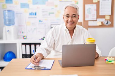 Middle age grey-haired man business worker using laptop writing on document at office