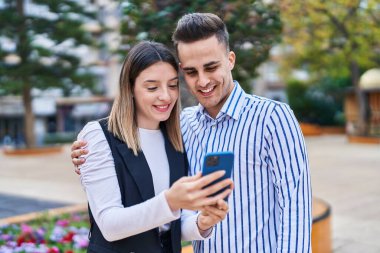 Man and woman couple hugging each other using smartphone at park