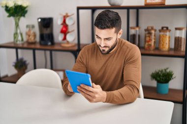 Young hispanic man using touchpad sitting on table at home